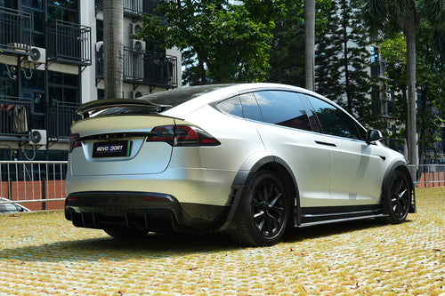 Silver Tesla Model X featuring a REVOZPORT body kit with carbon fiber front lip, side skirts, wide fender flares, and lowered stance parked outdoors in sunlight.