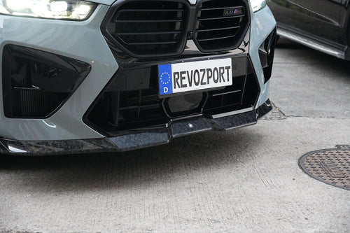 Gray BMW X6M featuring a REVOZPORT carbon fiber body kit with aggressive front lip, side skirts, and sporty aero styling parked on an urban street at dusk.