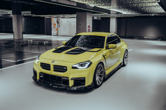 Yellow BMW with carbon fiber body kit parked in a modern garage, highlighting front lip, hood vents, and side skirt styling.