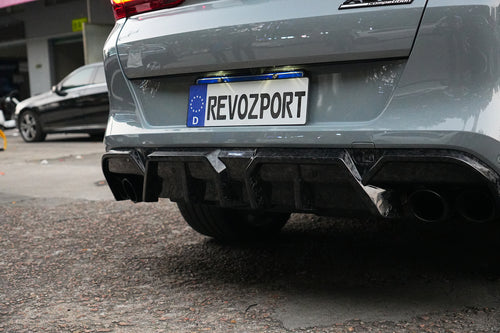 Gray BMW X6M featuring a REVOZPORT carbon fiber body kit with aggressive front lip, side skirts, and sporty aero styling parked on an urban street at dusk.