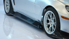 Close-up of a silver wide-body Chevrolet Corvette performance car displayed indoors, featuring aggressive aerodynamic bodywork, carbon fiber front splitter, vented hood, and lightweight multi-spoke wheels. The image highlights the custom motorsport styling and premium carbon fiber aero components under exhibition lighting.