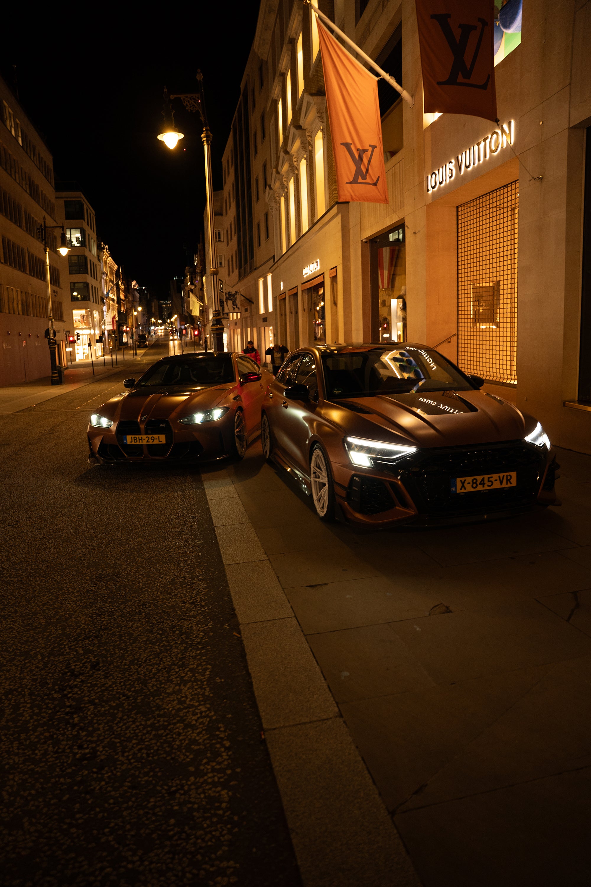 Bronze Audi RS4 Avant featuring a REVOZPORT carbon fiber body kit with front lip and side skirts, paired with silver multi-spoke forged wheels, parked in a modern urban setting.