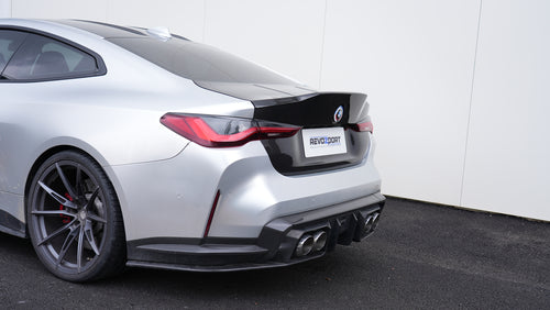 Close-up of a BMW G82 M4 rear end featuring a REVOZPORT carbon fiber trunk lid and integrated carbon rear spoiler, highlighting the glossy carbon weave detail.
