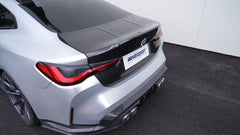Close-up of a BMW G82 M4 rear end featuring a REVOZPORT carbon fiber trunk lid and integrated carbon rear spoiler, highlighting the glossy carbon weave detail.
