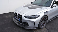 Silver BMW G82 M4 featuring a REVOZPORT carbon fiber body kit with front lip, side skirts, vented fenders, and aggressive aero styling parked outside a modern building.
