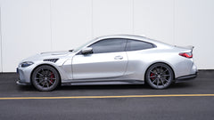 Silver BMW G82 M4 featuring a REVOZPORT carbon fiber body kit with front lip, side skirts, vented fenders, and aggressive aero styling parked outside a modern building.
