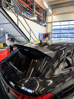 Black Audi RS3 Sportback featuring a REVOZPORT carbon fiber body kit with front lip and side skirts parked on a wet outdoor lot.