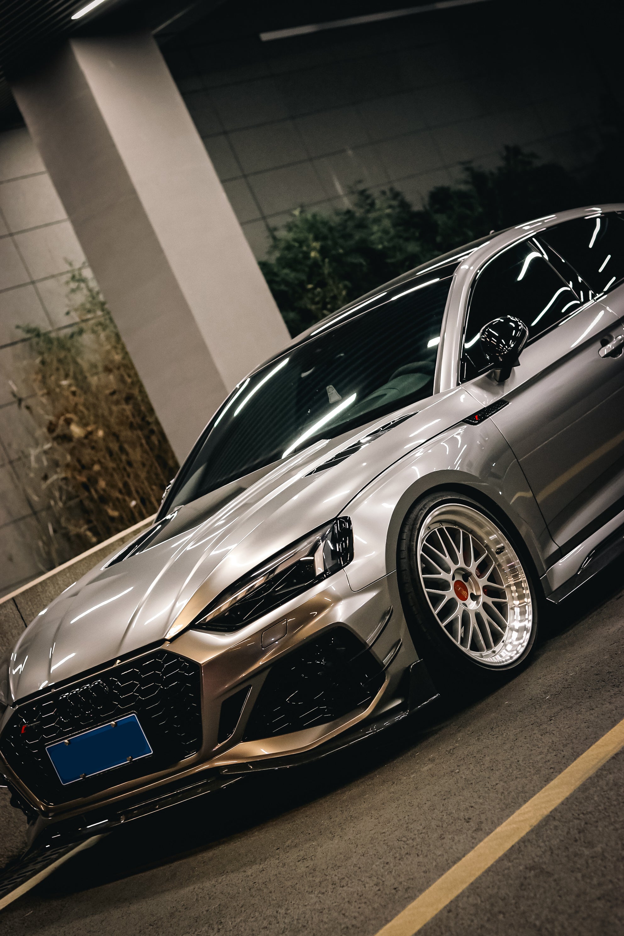 Top-down view of a gray Audi RS5 Sportback featuring a REVOZPORT carbon fiber body kit with vented hood, front lip, side skirts, and large rear wing driving through a dimly lit urban tunnel at night.