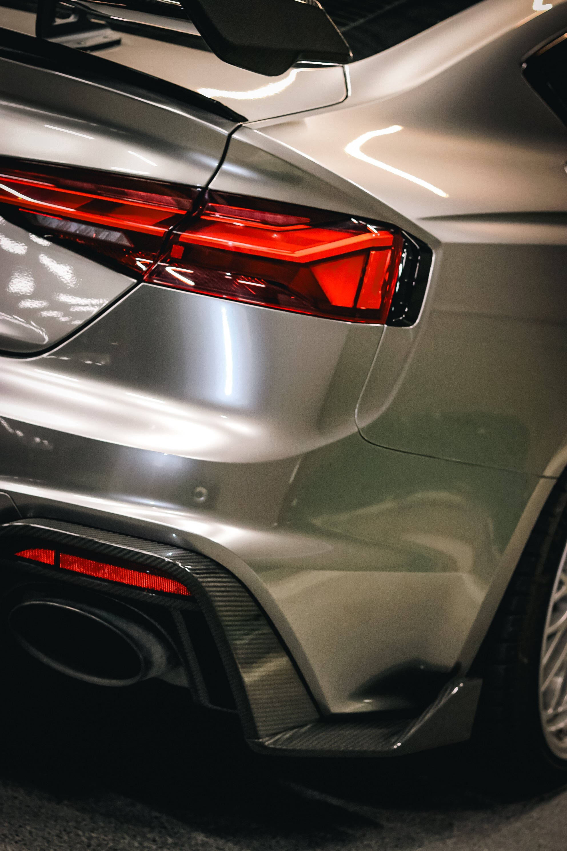 Top-down view of a gray Audi RS5 Sportback featuring a REVOZPORT carbon fiber body kit with vented hood, front lip, side skirts, and large rear wing driving through a dimly lit urban tunnel at night.