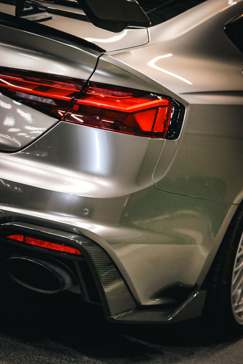 Top-down view of a gray Audi RS5 Sportback featuring a REVOZPORT carbon fiber body kit with vented hood, front lip, side skirts, and large rear wing driving through a dimly lit urban tunnel at night.