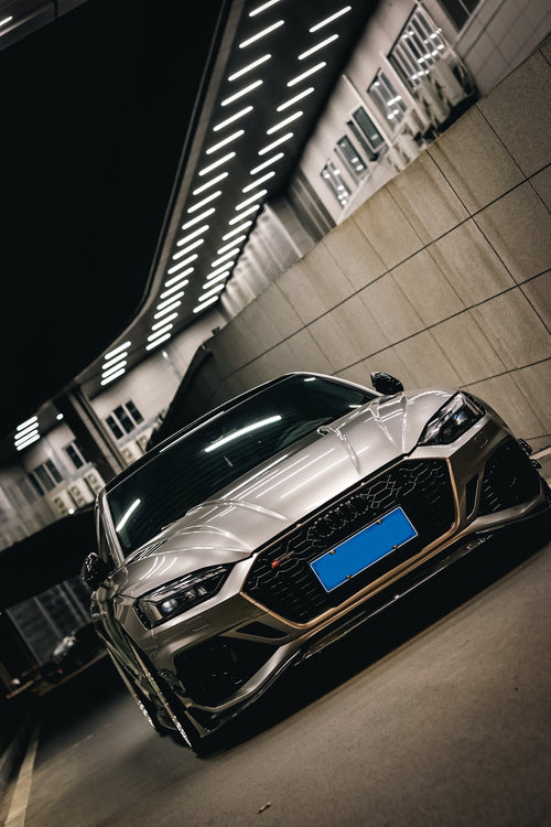 Top-down view of a gray Audi RS5 Sportback featuring a REVOZPORT carbon fiber body kit with vented hood, front lip, side skirts, and large rear wing driving through a dimly lit urban tunnel at night.