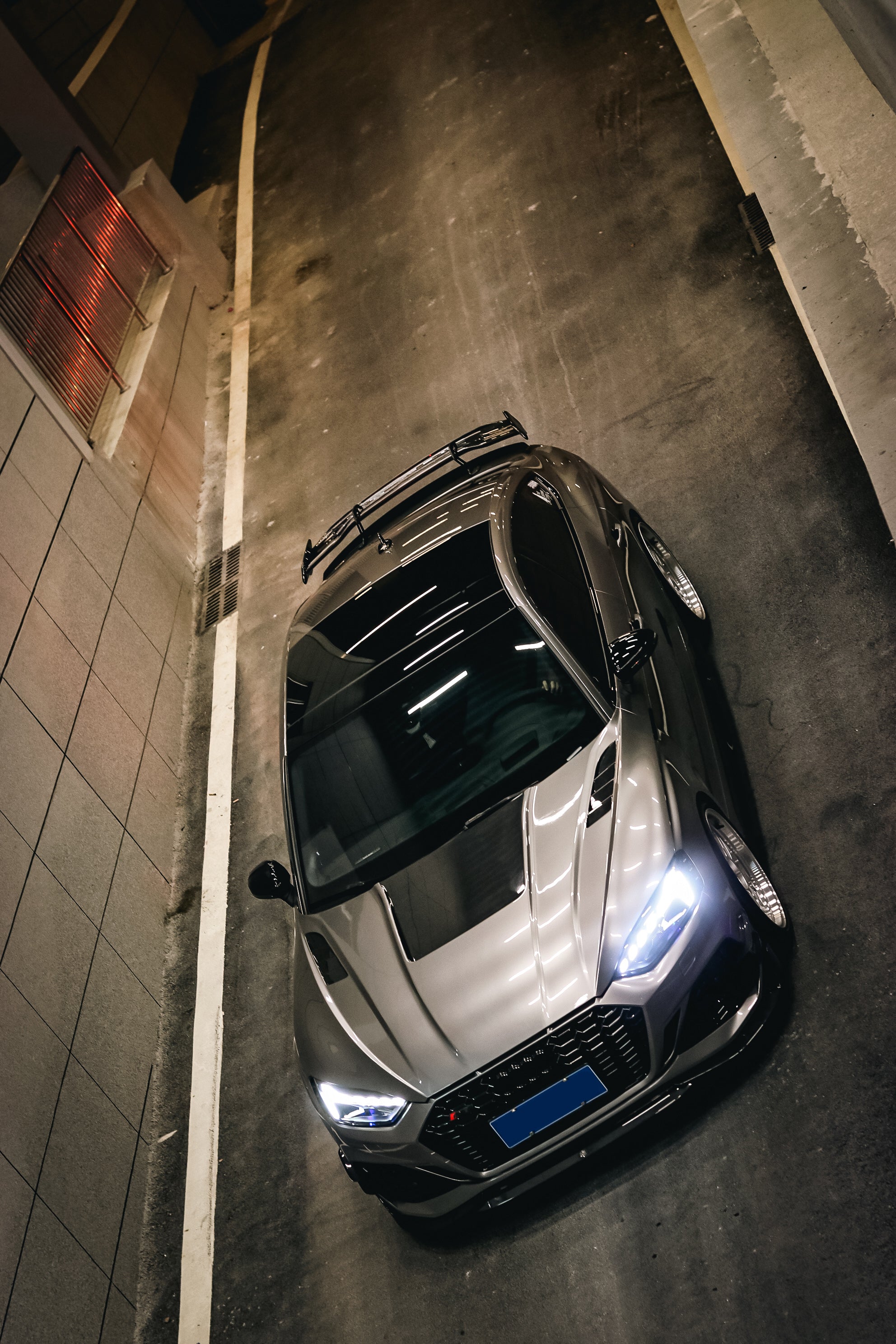 Top-down view of a gray Audi RS5 Sportback featuring a REVOZPORT carbon fiber body kit with vented hood, front lip, side skirts, and large rear wing driving through a dimly lit urban tunnel at night.