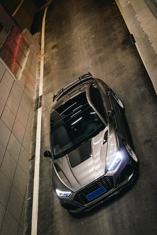 Top-down view of a gray Audi RS5 Sportback featuring a REVOZPORT carbon fiber body kit with vented hood, front lip, side skirts, and large rear wing driving through a dimly lit urban tunnel at night.