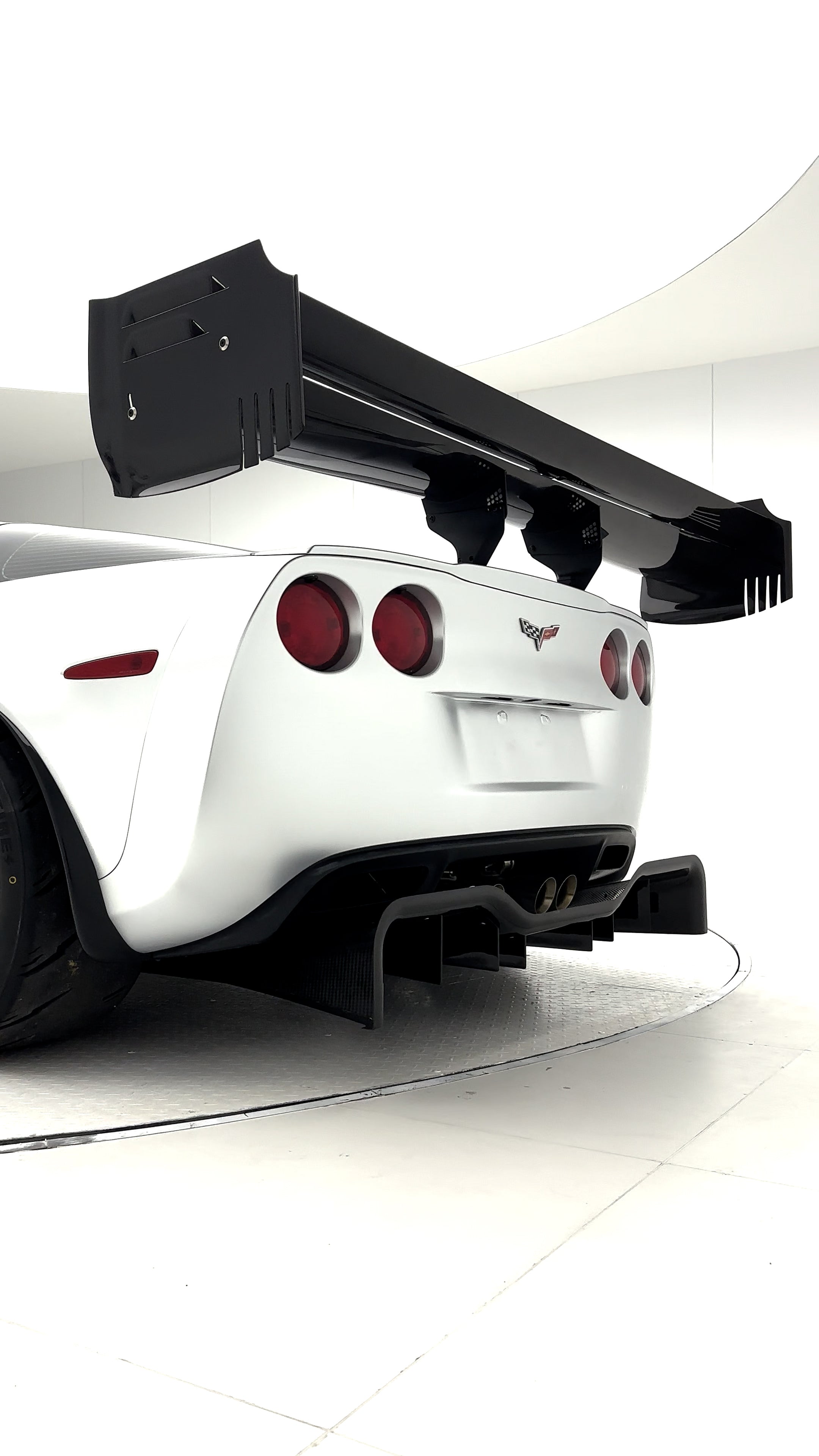 Close-up of a silver wide-body Chevrolet Corvette performance car displayed indoors, featuring aggressive aerodynamic bodywork, carbon fiber front splitter, vented hood, and lightweight multi-spoke wheels. The image highlights the custom motorsport styling and premium carbon fiber aero components under exhibition lighting.