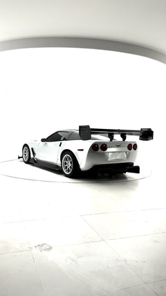 Close-up of a silver wide-body Chevrolet Corvette performance car displayed indoors, featuring aggressive aerodynamic bodywork, carbon fiber front splitter, vented hood, and lightweight multi-spoke wheels. The image highlights the custom motorsport styling and premium carbon fiber aero components under exhibition lighting.