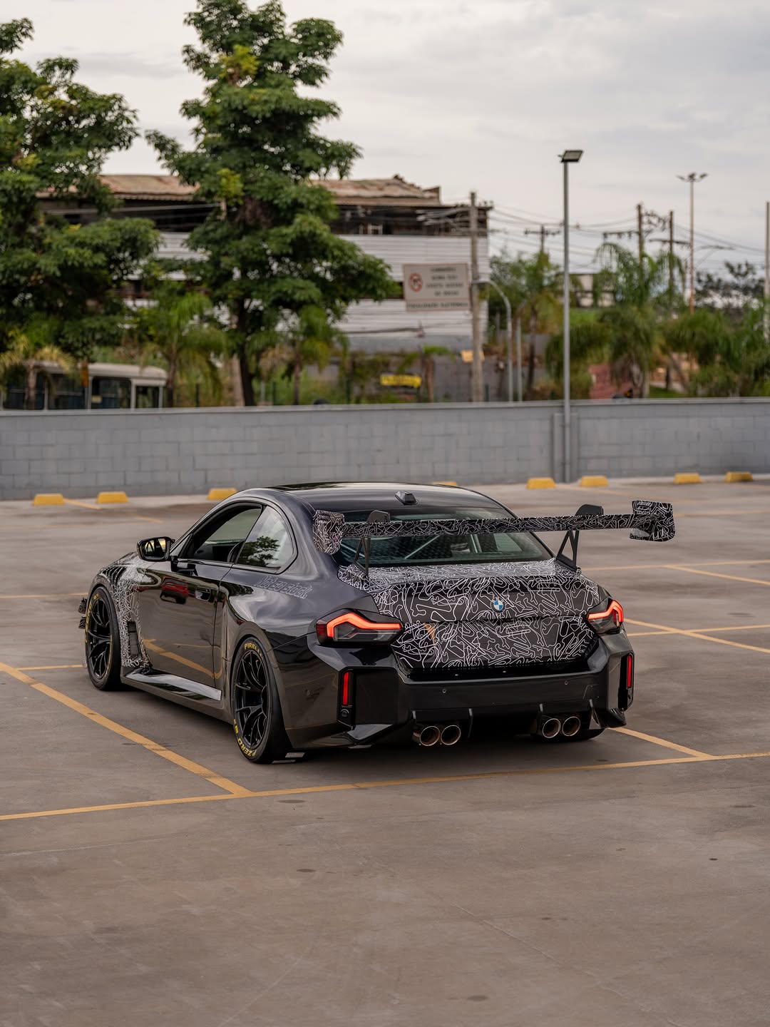 Gray BMW M2 featuring a REVOZPORT body kit with front lip, rear wing, canards, vented fenders, and hood, parked in an open rooftop lot.