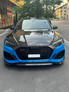 Blue Audi RS5 Sportback featuring a REVOZPORT carbon fiber body kit with vented hood, front lip, side skirts, and lowered stance parked outside a modern industrial building at sunset.