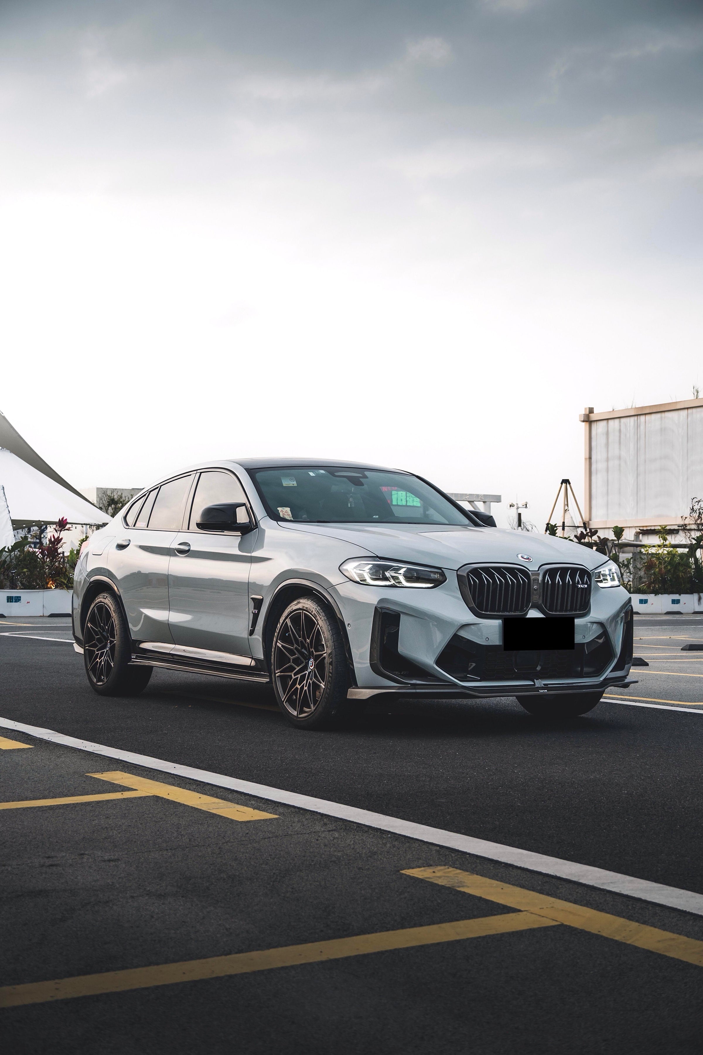 White BMW X4M featuring a REVOZPORT front grille upgrade and sporty front-end styling parked on an open urban road.