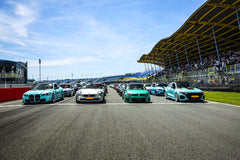 Multiple modified performance cars lined up on a racetrack grid, showcasing carbon fiber aero styling at a motorsport event.